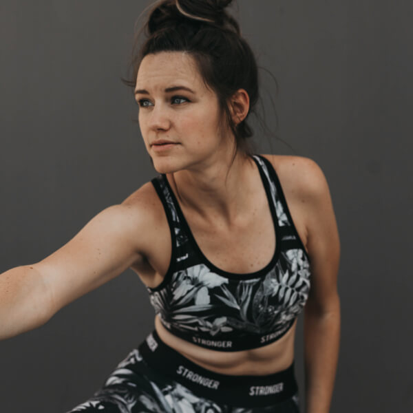 Young woman with dark hair in a messy bun dressed in a black and white cropped gym outfit, stretching