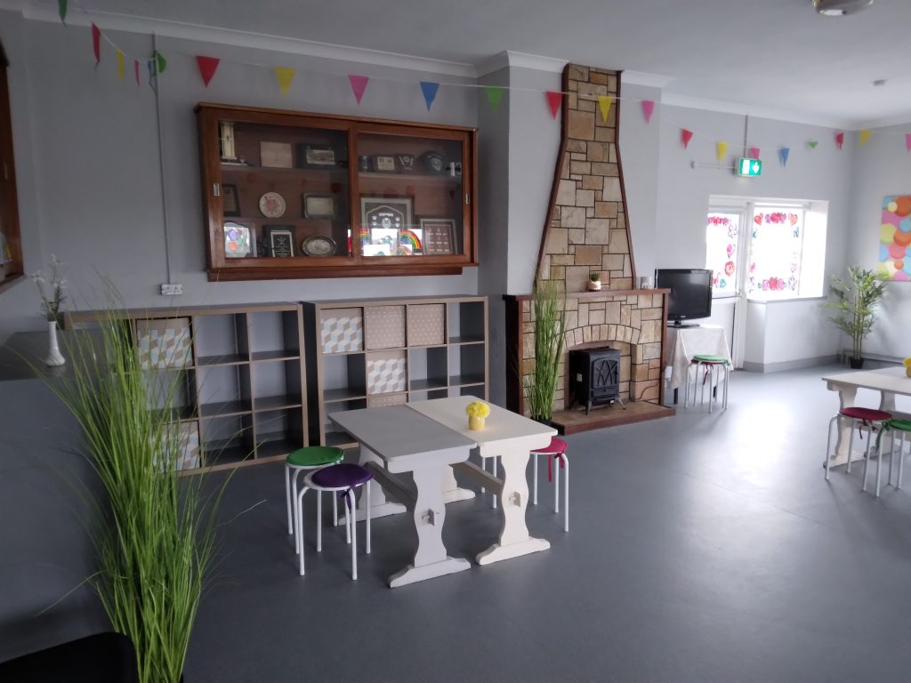 two party tables in grey and cream and chairs in front of Kallex units. fireplace to the right of the image and colourful bunting at the top of the wall close to the ceiling. 