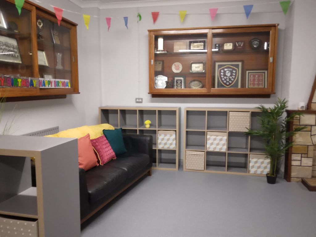 Function room image with black couch on the left with cushions, ikea kallex shelving and  trophy cabinets above the kallex units and couch. 
