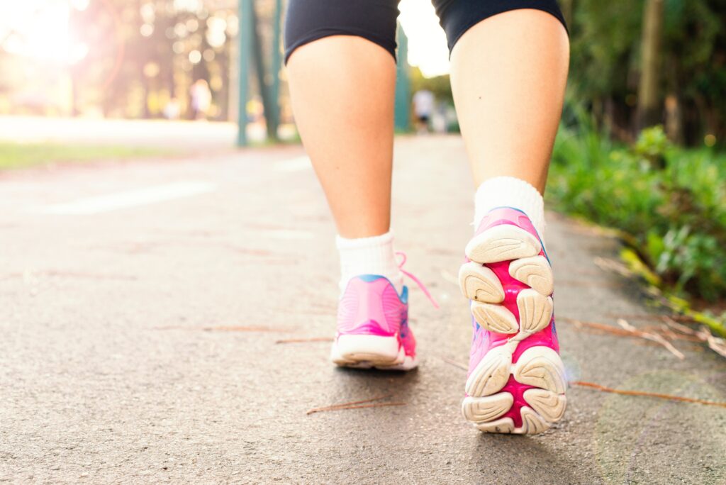 image of the lower half of a womans pair of legs, with pink runners walking on a path with grass in the background