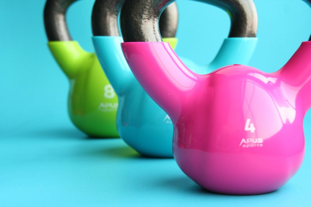 Three coloured kettle bells (pink, blue and green) in a row with a blue background